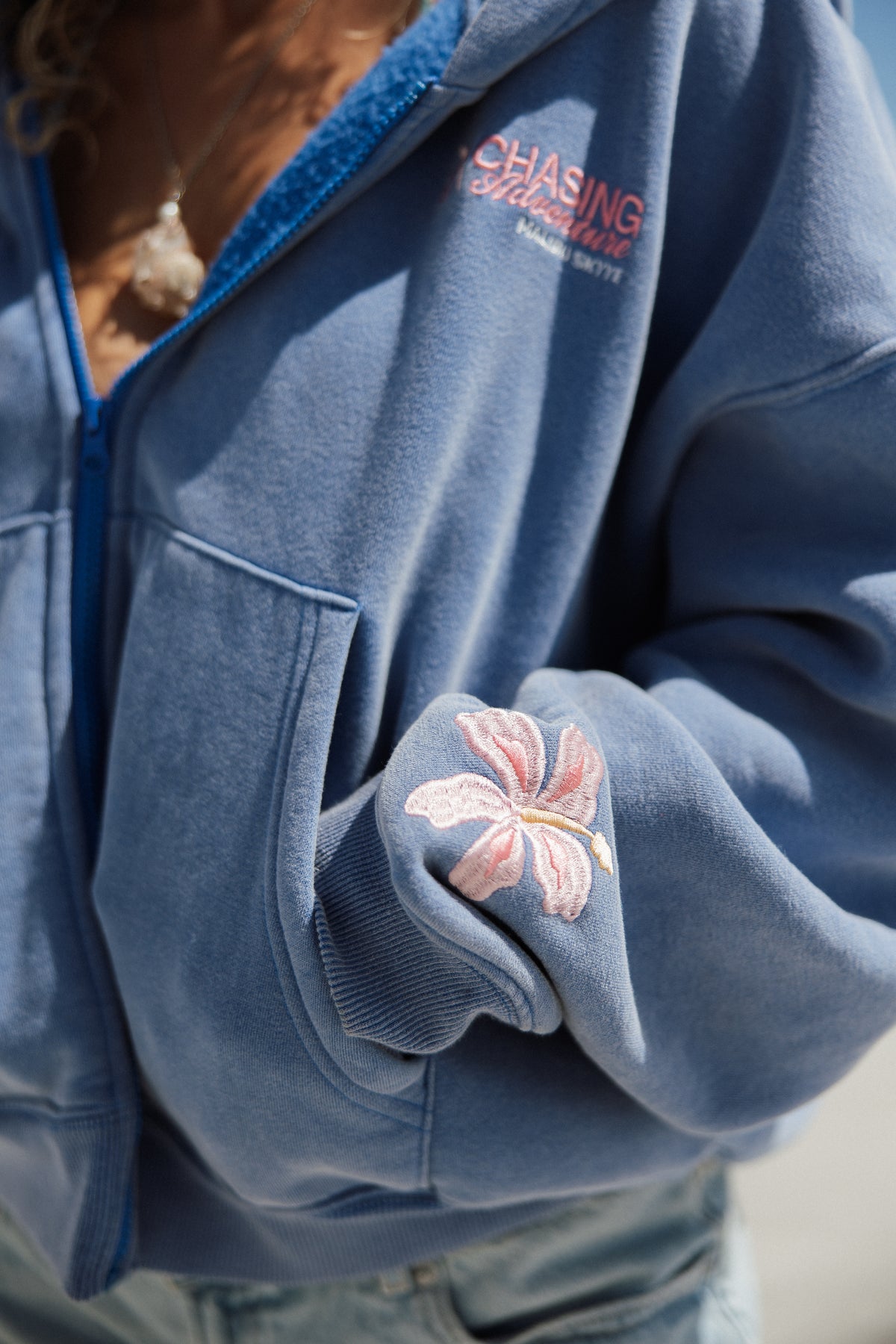 Blue jacket with floral embroidery on sleeve and 'Chasing Adventures' logo.