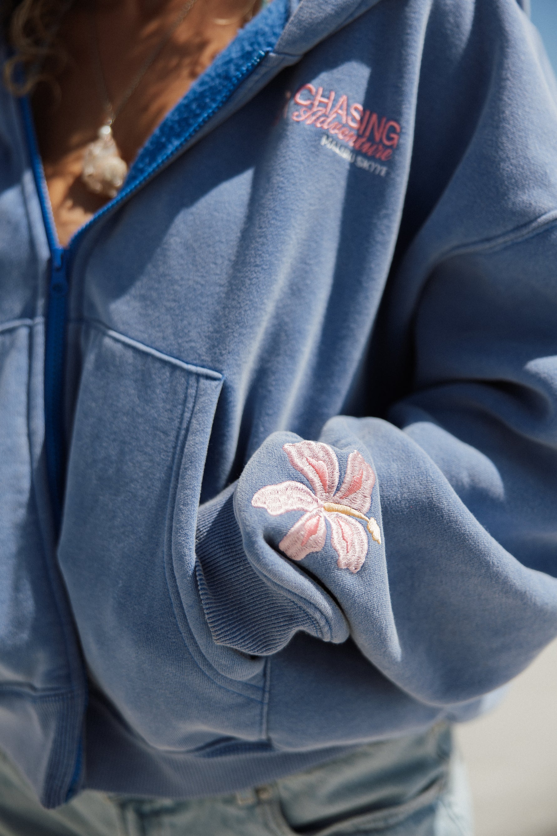 Blue jacket with floral embroidery on sleeve and 'Chasing Adventures' logo.